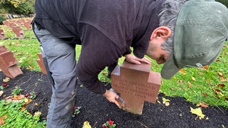 Ein Mann putzt vor Allerheiligen auf dem Hauptfriedhof in Karlsruhe einen Grabstein.
