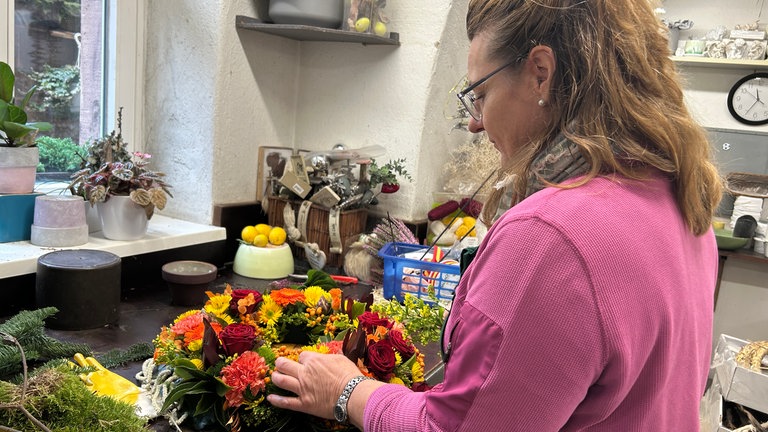 Eine Frau richtet vor Allerheiligen Grabschmuck aus Blumen auf dem Hauptfriedhof in Karlsruhe.