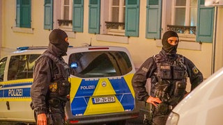 Zwei Bundespolizisten stehen vor einem Polizeiauto in der Innenstadt von Baden-Baden. In Baden-Baden und anderen Orten in Baden-Württemberg fanden bis in die Nacht hinein großflächige Duchsuchungen mehrerer Gebäude statt. 