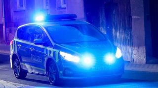 Symbolbild: Ein Fahrzeug der Polizei fährt mit Blaulicht am Abend durch eine Straße. Bei einer Durchsuchung in einem Spielcasino in Calw sind nach Polizeiangaben hat die Polizei zwei scharfe Schusswaffen sichergestellt. 