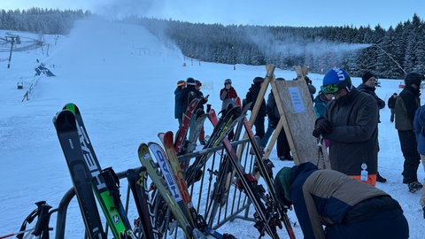 Skifahrer sammeln sich am Ende der Piste am Mehliskopf. Im Hintergrund laufen die Schneekanonen.