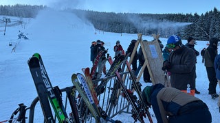 Skifahrer sammeln sich am Ende der Piste am Mehliskopf. Im Hintergrund laufen die Schneekanonen.