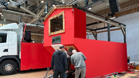 In der Karlsruher Gartenhalle bauen mehrere Männer an einem Wagen für den Fastnachtsumzug.