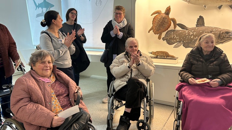 Demenzpatienten und Betreuer klatschen am Ende der Führung im Naturkundemuseum Karlsruhe. 
