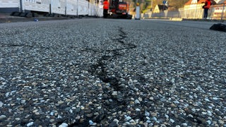Ein Riss auf Asphalt, der bis zu einem Baustellenfahrzeug verläuft. Auf der B462 bei Forbach wird gebaut. 