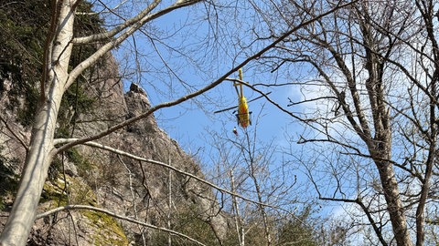 Ein gelber Rettungshubschrauber schwebt über einer Felswand