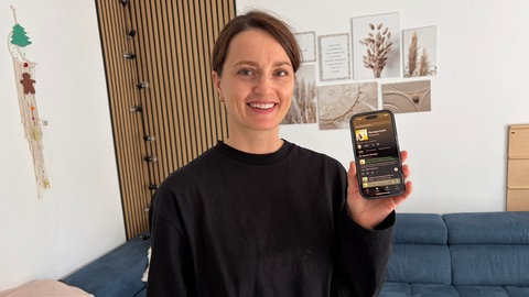 Eine Frau im schwarzen Pullover hält ein Handy hoch