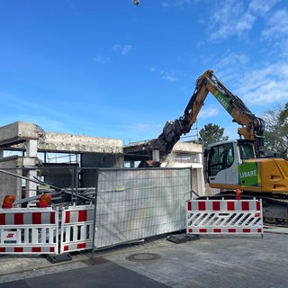 Abriss Turmbergbahn in Karlsruhe-Durlach: Ein gelber Bagger reißt ein Stück aus dem Gerippe eines grauen Betongebäudes.
