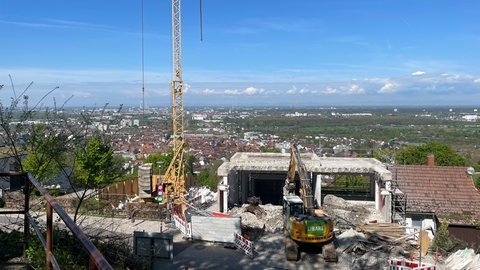 Abriss Turmbergbahn: Ein gelber Bagger reißt ein Stück aus dem Gerippe eines grauen Betongebäudes mit Blick auf Karlsruhe-Durlach.