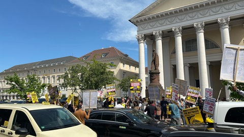 Auf dem Karlsruher Marktplatz stehen wegen einer Demo mehrere Taxis. Mehr als 100 Menschen demonstrieren für strengere Regeln für Mietwagenunternehmen, die mit Uber, Wolt und Co. zusammenarbeiten.