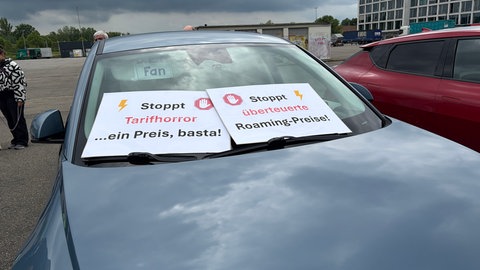 Auto mit Plakaten hinter der Windschutzscheibe, die vermeintlich undurchsichtige Ladetarif- und Bezahlarten kritisieren.