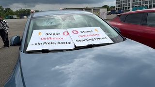 Auto mit Plakaten hinter der Windschutzscheibe, die vermeintlich undurchsichtige Ladetarif- und Bezahlarten kritisieren.