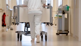 (Symbolbild) Eine Krankenpflegerin schiebt ein Krankenbett durch einen Flur einer Klinik.