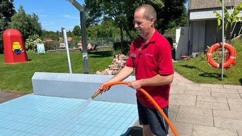Ein Mann spritzt die Duschen im Freibad in Karlsruhe ab
