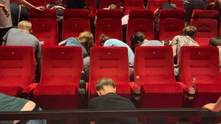 Menschen schrauben im Kinosaal In Schauburg in Karlsruhe Kinosessel ab.