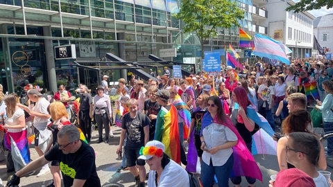 Teilnehmende der CSD-Demo laufen durch die Straßen in Karlsruhe. Viele haben sich bunte Fahnen umgehängt.