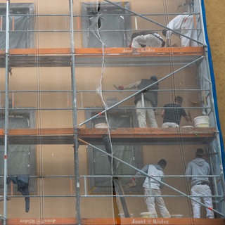 (Symbolbild) Arbeiter auf einem Baugerüst verrichten Arbeiten an der Fassade eines Hauses. Eine Plattform von Forschenden des KIT in Karlsruhe soll bei der Planung für Sanierungen helfen.