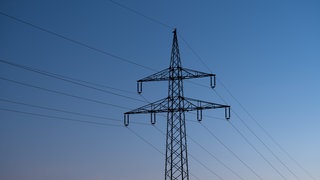 (Symbolbild) Ein Strommast ist bei Sonnenaufgang als Silhouette zu sehen. In Baden-Baden ist der Strom ausgefallen.