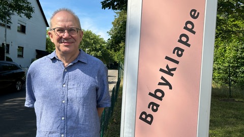 Michael Schröper, der Gründer der Babyklappe in Karlsruhe, steht vor einem Schild.