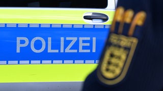 Symbolbild Festnahme: Polizeifahrzeug und Arm eines Polizeibeamten