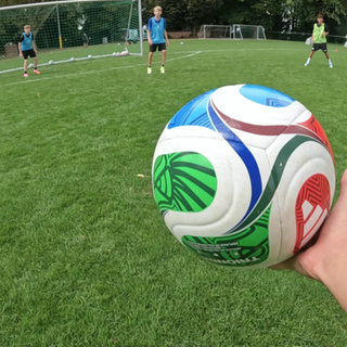 Eine Hand hält vor dem Tor einen Fußball. Im Hintergrund sind zwei Jugendliche. Durch den Wegfall verschiedener Regeln, sollen sie den Sinn von ihnen lernen.