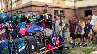 Die Kinder stehen Schlange vor einem Haufen Schulränzen.