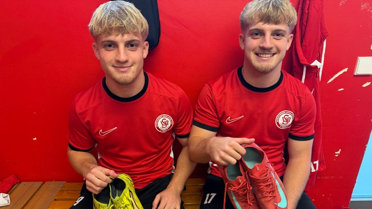 Zwillinge zeigen ihre verschiedenfarbige Fußballschuhe.
