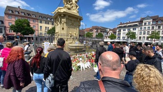 Menschen auf dem Marktplatz in Mannheim am Brunnen mit Blumen und Kerzen trauern um toten Polizisten