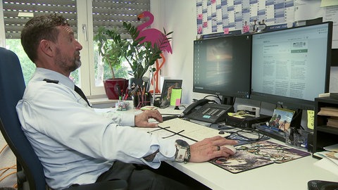 Polizist am Schreibtisch vor Bildschirmen