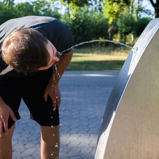 Mann steht gebückt vor Trinkwasserbrunnen und trinkt
