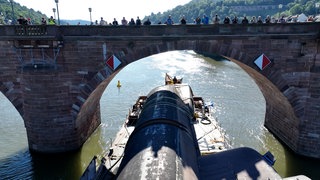 U-Boot fährt unter der Alten Brücke in Heidelberg durch. Auf der Neckarbrücke stehen zahlreiche Menschen
