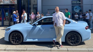 Ein Autposer steht in Mannheim vor seinem blauen Wagen