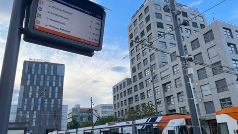 Vor dem Mannheimer Hauptbahnhof steht eine Straßenbahn und eine Anzeigetafel zeigt die nächsten Verbindungen.