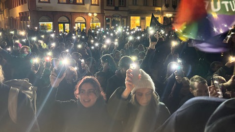 Menschen mit Handys und Lichtern auf dem Heidelberger Marktplatz nach Demomstration gegen CDU und AfD