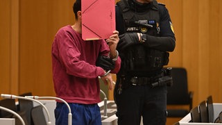 Sulaiman A. bedeckt sein Gesicht mit einem roten Ordner im Sitzungssaal des Oberlandesgerichts