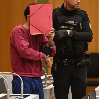 Sulaiman A. bedeckt sein Gesicht mit einem roten Ordner im Sitzungssaal des Oberlandesgerichts