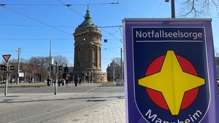 Im Hintergrund sieht man den Mannheimer Wasserturm. Davor steht ein Banner von der Notfallseelsorge Mannnheim.