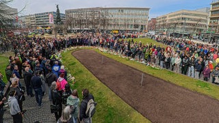 Menschen stehen bei dem interreligiösen Gebet auf dem Paradeplatz in Mannheim zusammen.