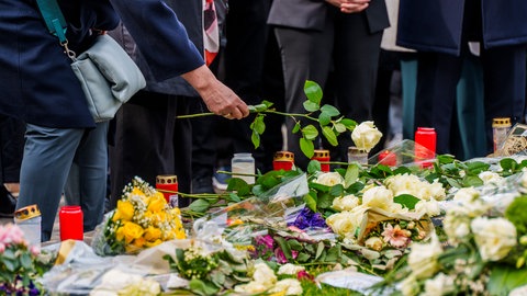 Menschen legen Blumen und Kerzen nieder.