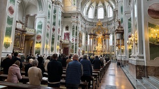 Gottesdienst in der Jesuitenkirche in Mannheim. Menschen stehen an ihren Plätzen.