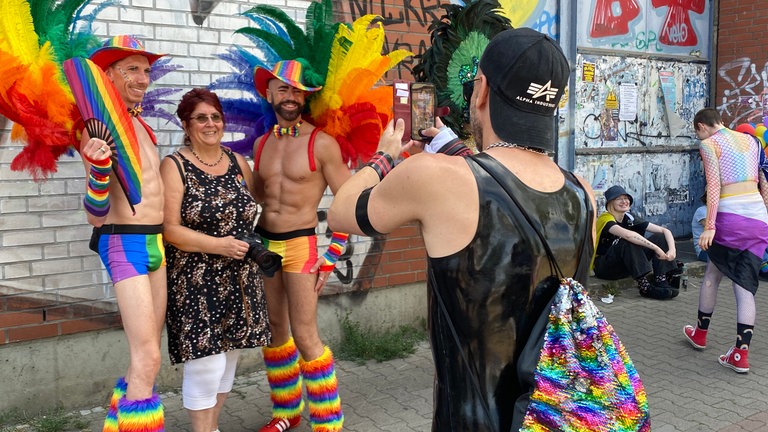 Eine Frau lässt sich zwischen zwei bunt gekleideten Männern fotografieren