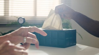 Hand eines Patienten, der ein Taschentuch aus einer Box auf einem Schreibtisch in einem Büro zieht.