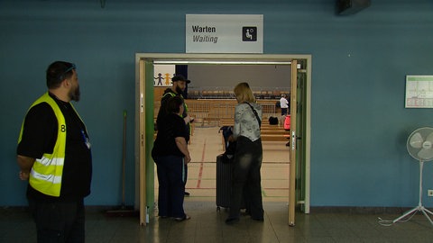 Eine Geflüchtete wird von drei Sicherheitsbeamten durch die Tür der Ankunftshalle geleitet. 