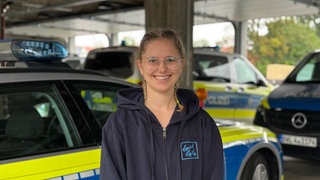 Teilnehmerin Anna steht vor einem Polizeiauto