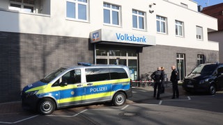 Zwei Autos der Polizei und mehrere Polizisten stehen vor einer Bankfiliale