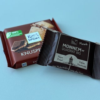 Eine Tafel Ritter Sport liegt neben einem Haferriegel von Wacker