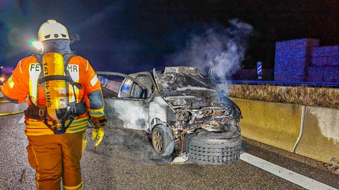 Das verunfallte Auto raucht noch, nachdem der Motor brannte. Unter der Motorhaube ein LKW-Reifen, im Vordergrund eine Feuerwehrperson.