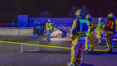 Im Hintergrund ein rauchendes Auto, im Vordergrund mehrere Feuerwehrmenschen. Aufgrund der Fahrbahnschäden, die auch durch einen weiteren Unfall verursacht wurden, dauert die Sperrung der A6 Richtung Heilbronn länger.