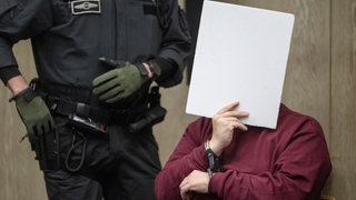 Der Angeklagte im Mordprozess kurz vor der Urteilsverkündung mit einer Mappe vor dem Gesicht