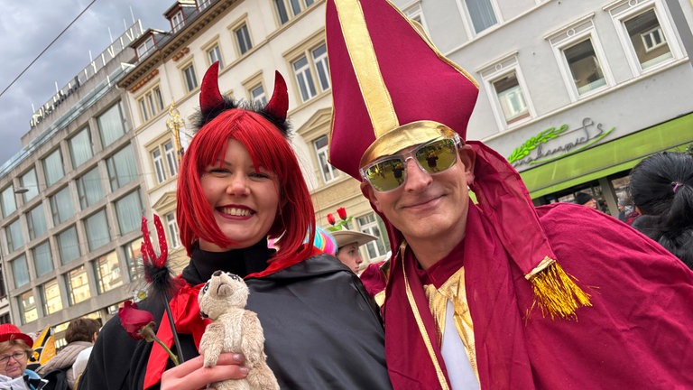 Teufelchen und Priester feiern gut gelaunt Seite an Seite.